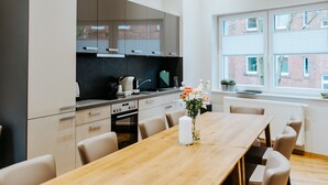 A modern kitchen with a large wooden table and chairs, a built-in oven, and a window overlooking a brick building. - Gerberhof (Erfurt)