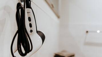 Un sèche-cheveux blanc avec un cordon noir qui pend à un mur.