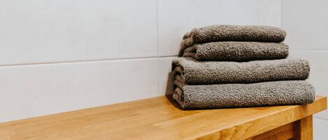 A stack of folded towels on a wooden bench against a tiled wall.