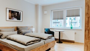 A modern bedroom with a wooden bed, a framed picture on the wall, a chair, and a window with blinds. - Gerberhof (Erfurt)