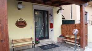 A hotel entrance with a wooden bench, a doormat, and a signboard. - Piccolo Hotel (Rosignano Marittimo)