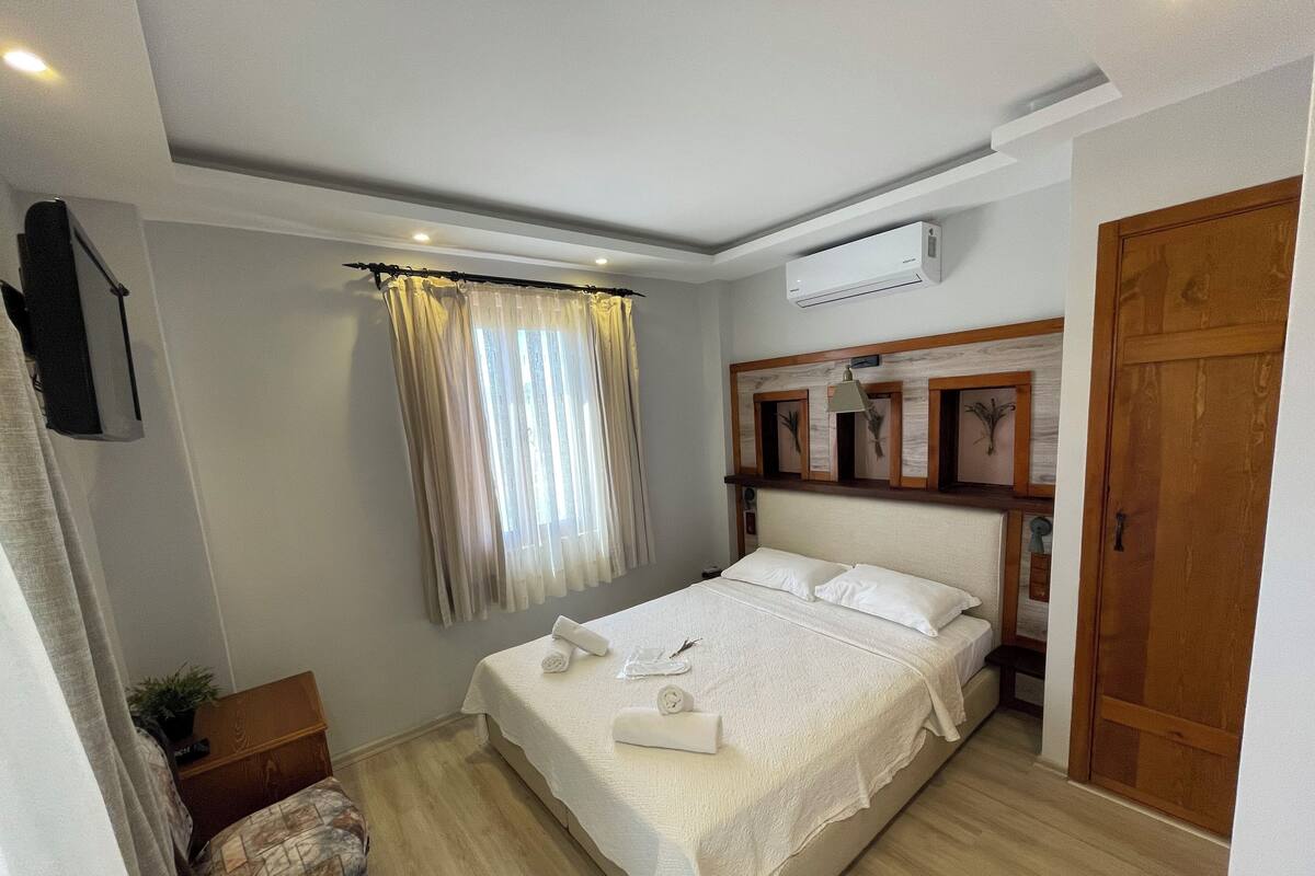 A neatly arranged bedroom with a bed, a bedside table, a chair, and an air conditioning unit.