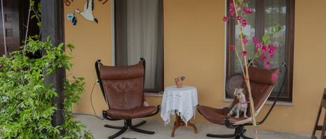A small outdoor seating area with two brown leather chairs, a small table with a white cloth, and a potted plant.