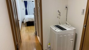 Une chambre d’hôtel avec un lit, un petit radiateur et une bouteille de gel hydroalcoolique posée sur le sol.