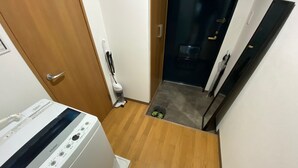 Une buanderie équipée d’un lave-linge à chargement frontal, d’un aspirateur et d’une paire de chaussures posées sur le sol.
