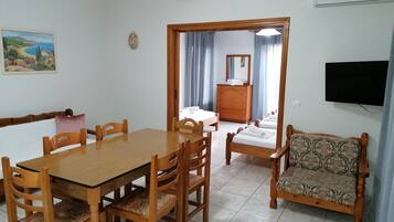 Una habitació amb taula de dinar de fusta, cadires, sofà, llit, prestatge i televisió.