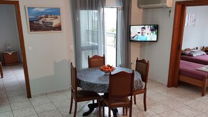 Ein Essbereich mit Tisch, Stühlen und Deckenventilator. Ein Fernseher ist an der Wand befestigt und ein Fenster mit Vorhängen vorhanden.