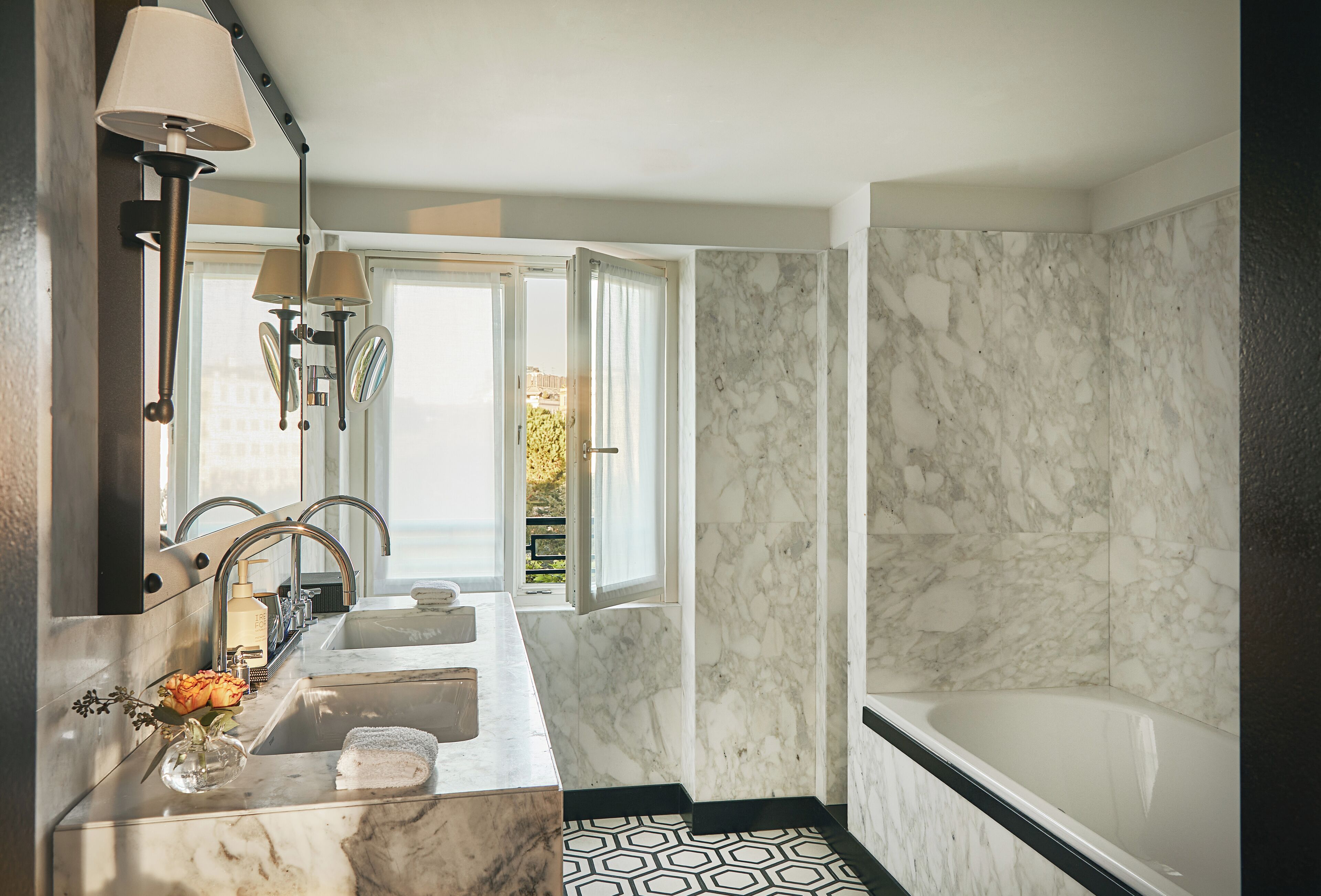 Un bagno con un lavabo in marmo, una vasca da bagno e un'ampia finestra con tende.