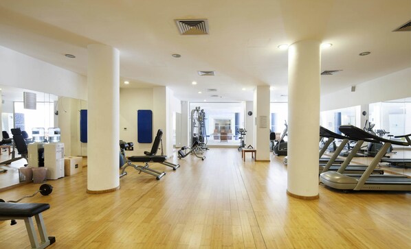 Un gimnasio con pisos de madera, equipo de ejercicio y amplias ventanas.