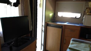 A compact kitchenette with a sink, a small refrigerator, and a television on a stand. - Camping A La Ferme De Cornaton (Confrancon)