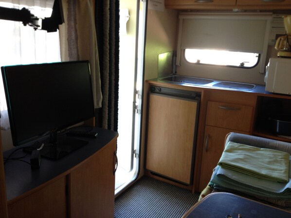 A compact kitchenette with a sink, a small refrigerator, and a television on a stand.