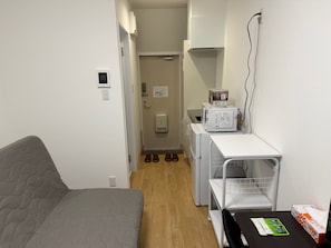 Habitación compacta con sofá gris, una mesita con caja de pañuelos, microondas y dispensador de agua.