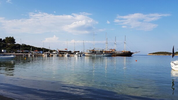 A marina with several boats docked, calm water, and a clear sky.