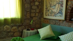 A room with a stone wall, a bed with green bedding, a painting, and a window with curtains.