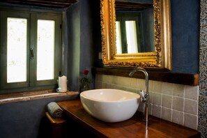 A bathroom with a white sink, a mirror with an ornate gold frame, and a window with green shutters.