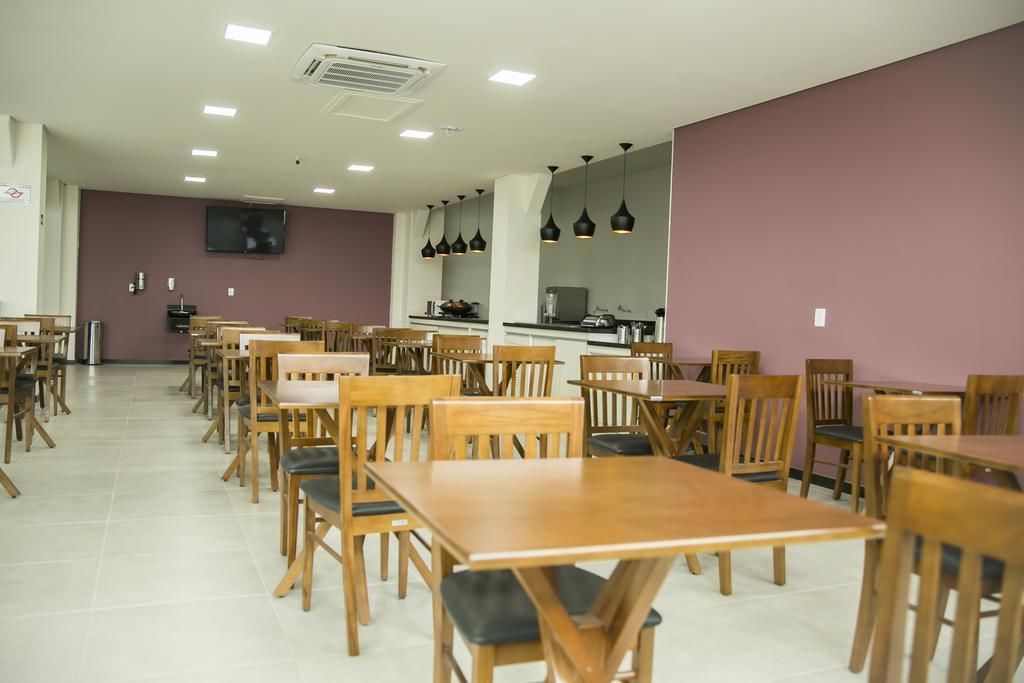A spacious dining area with multiple wooden tables and chairs, a kitchen counter, and pendant lighting.