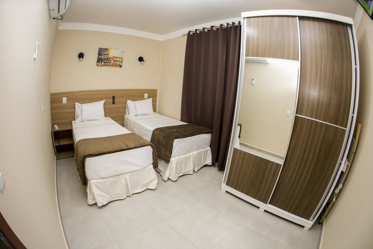 Habitación de hotel con dos camas, un armario y aire acondicionado instalado en la pared.
