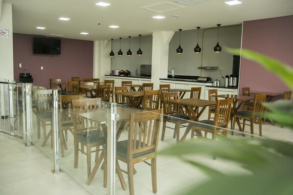 Comedor con varias mesas y sillas, zona de cocina con electrodomésticos e iluminación colgante.