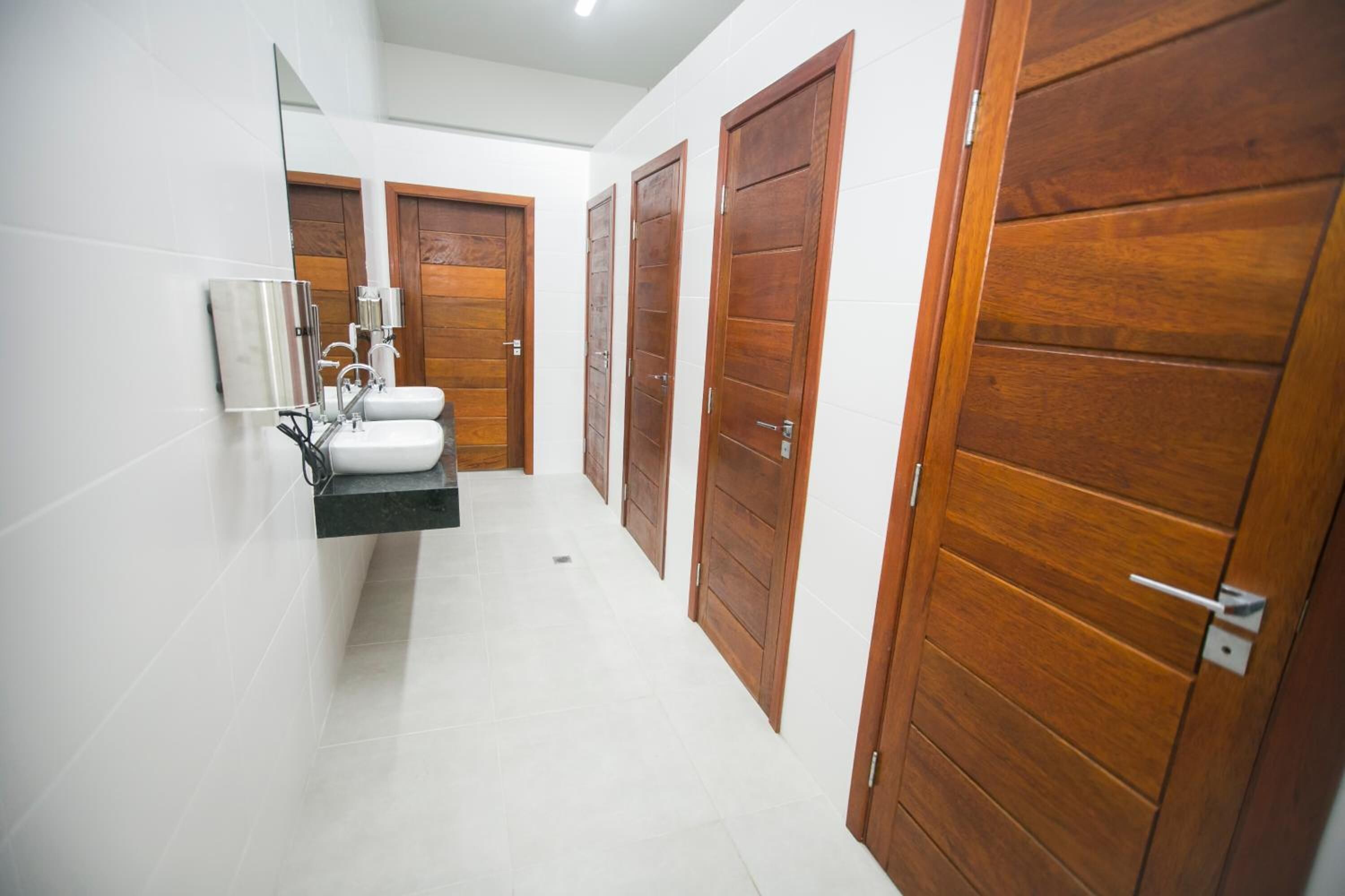 A modern bathroom with a white tiled floor, a black sink, and wooden doors.