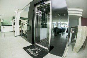 Entrada de ascensor con puerta de cristal y felpudo con el nombre del hotel.