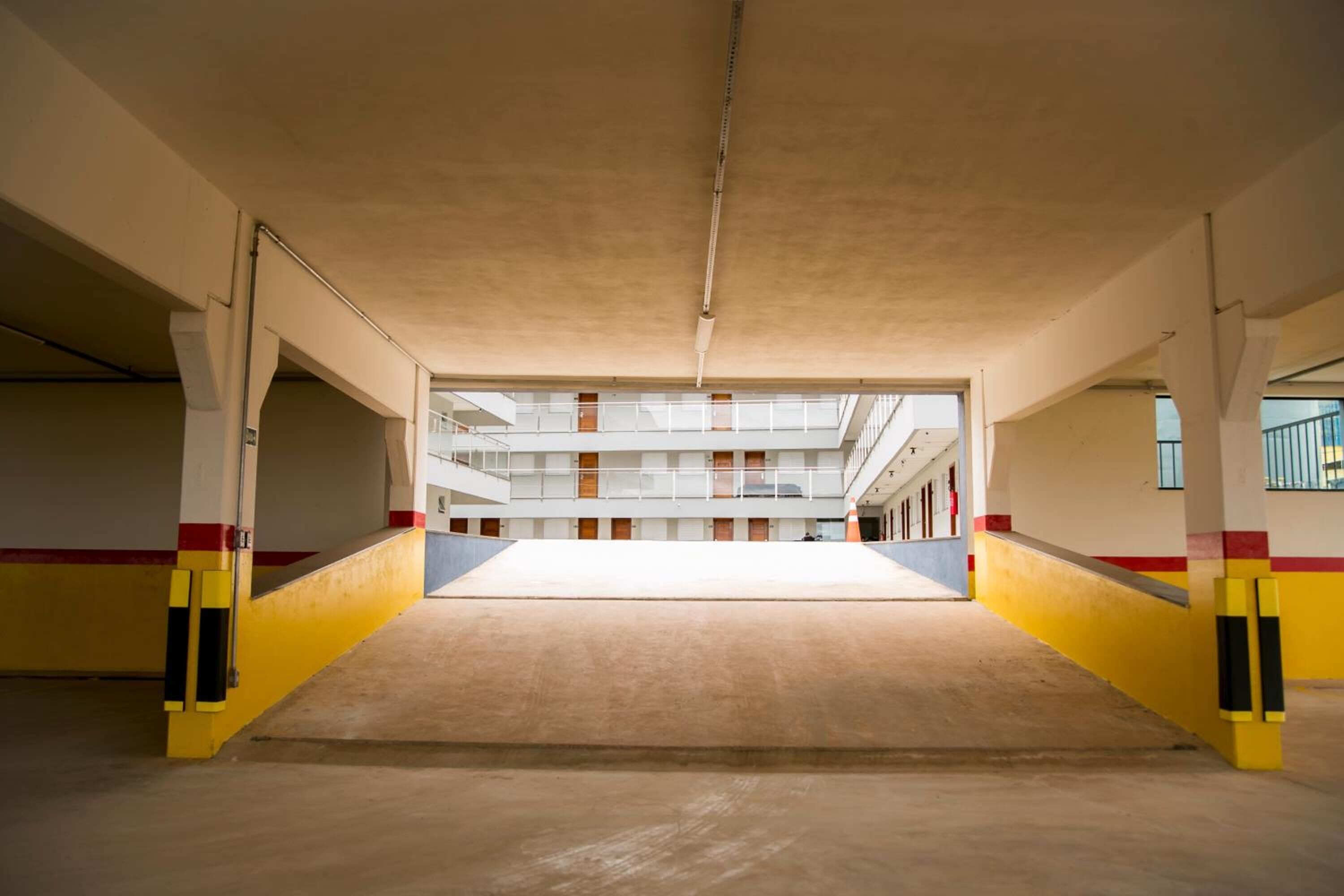 Un estacionamiento interior con un espacio central abierto, piso de concreto y pilares amarillos y rojos.