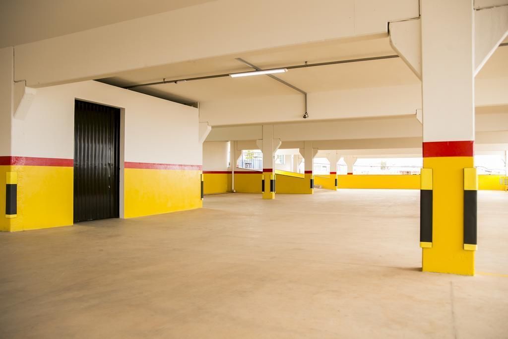 Amplio estacionamiento interior con paredes y columnas pintadas de amarillo y rojo, destacando una puerta negra y vigas estructurales visibles.