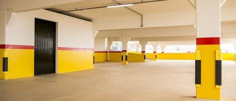 Amplio estacionamiento interior con paredes y columnas pintadas de amarillo y rojo, destacando una puerta negra y vigas estructurales visibles.