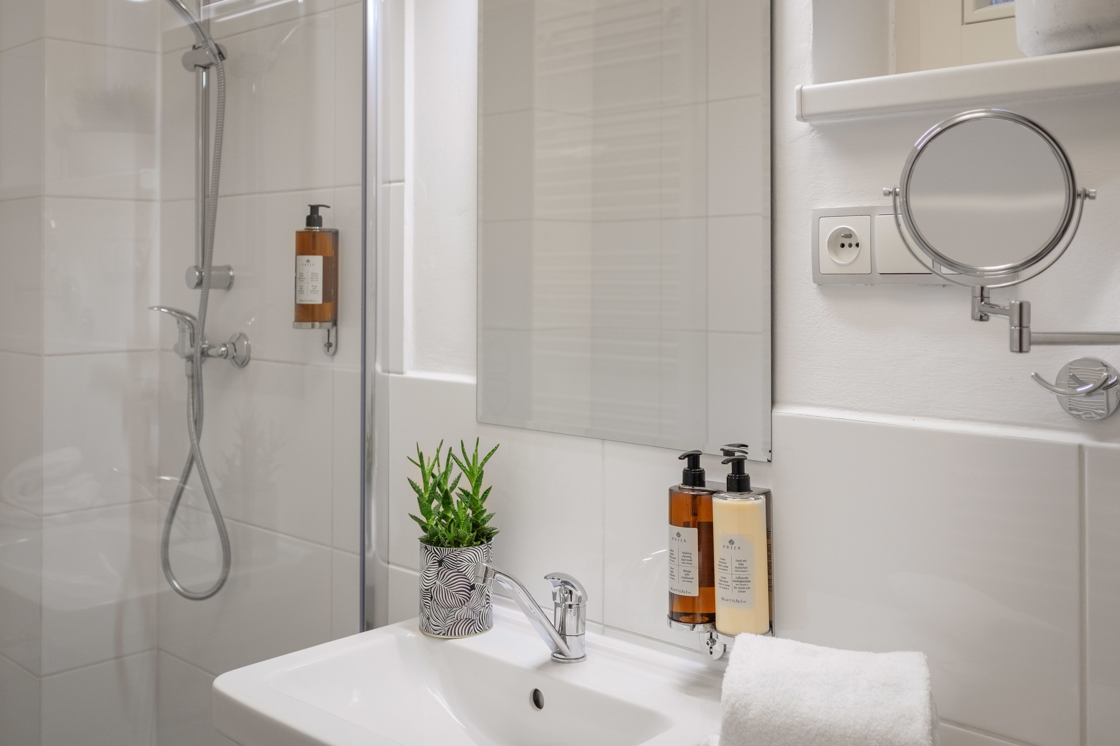 A modern bathroom with a glass shower enclosure, a white sink with a mirror, and toiletries on the wall.