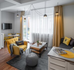 A modern living room with a sofa, armchair, coffee table, and a TV mounted on the wall. - City Leaf Apartments (Prague)