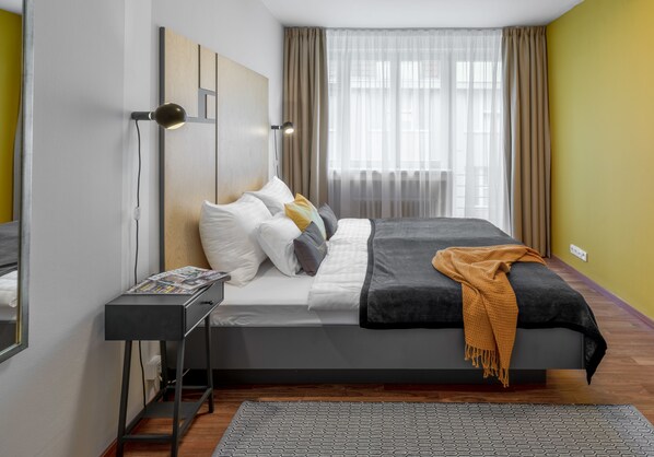 A neatly arranged bedroom with a bed, bedside table, lamp, and a window with curtains. - City Leaf Apartments (Prague)