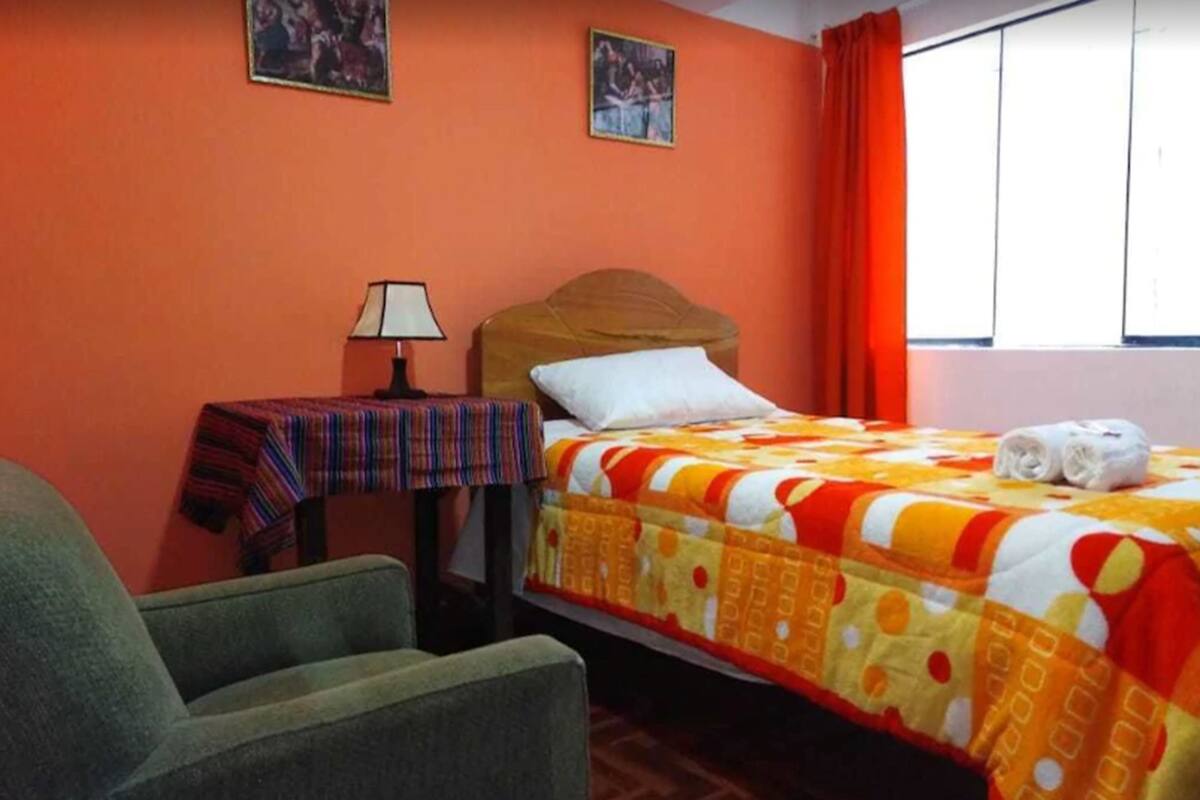 Une chambre d’hôtel avec un lit, une chaise, une table avec une lampe et deux tableaux encadrés au mur.