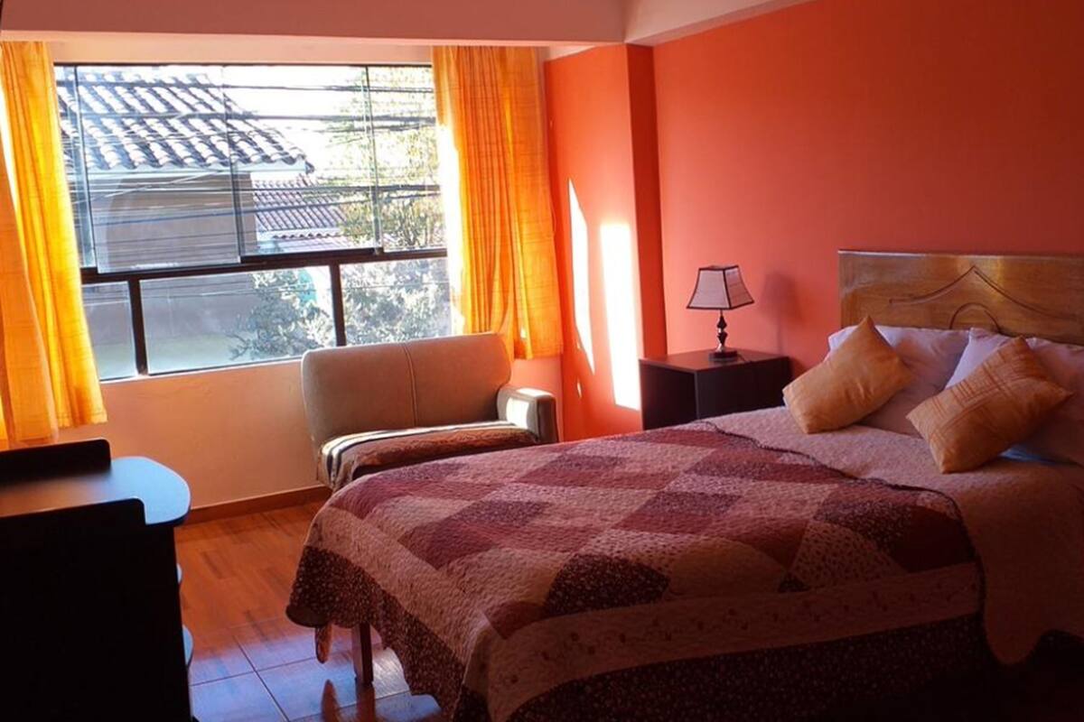 Une chambre à coucher avec un lit, une table de chevet, une chaise et une fenêtre avec des rideaux.