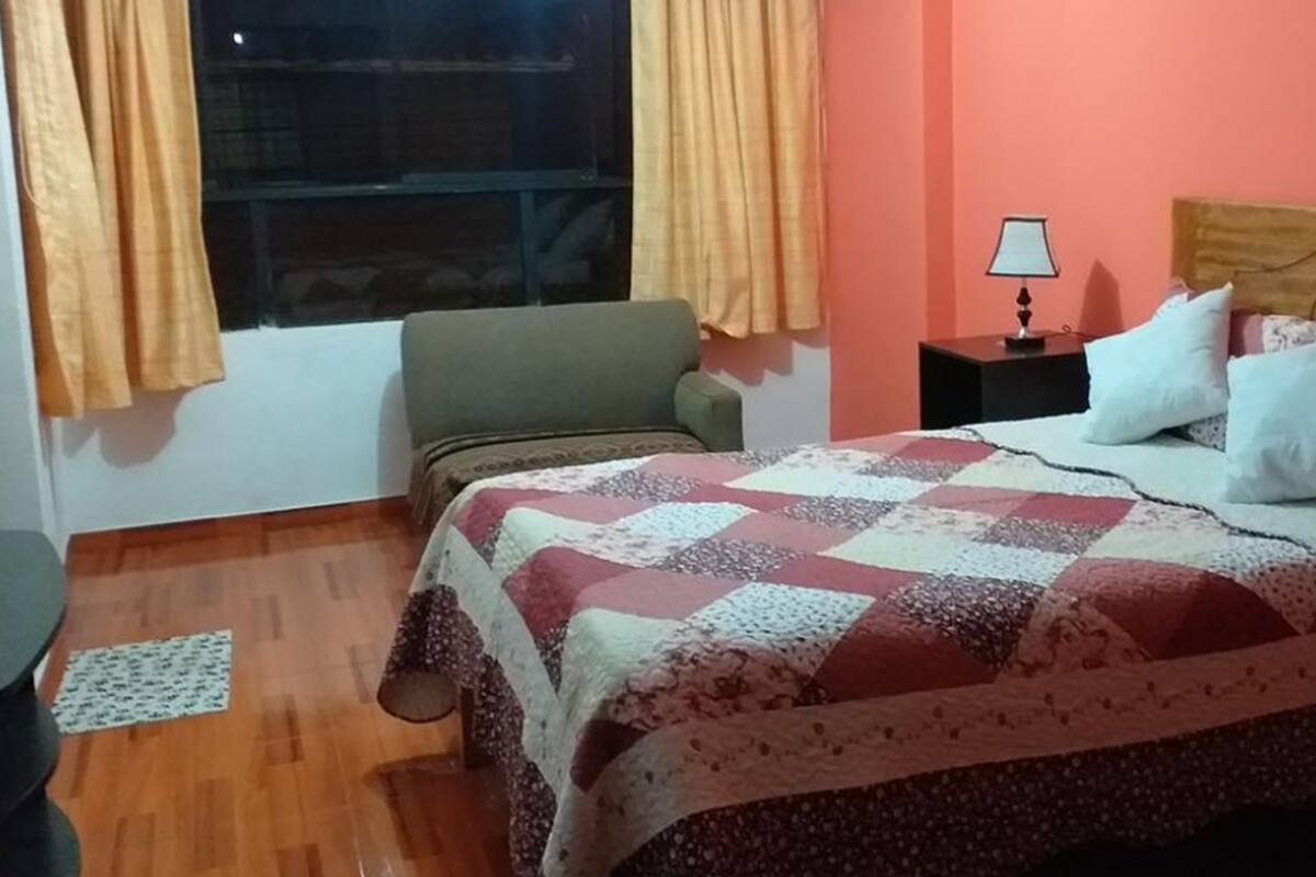 Une chambre à coucher avec un lit, une table de chevet, une chaise et une fenêtre avec des rideaux.