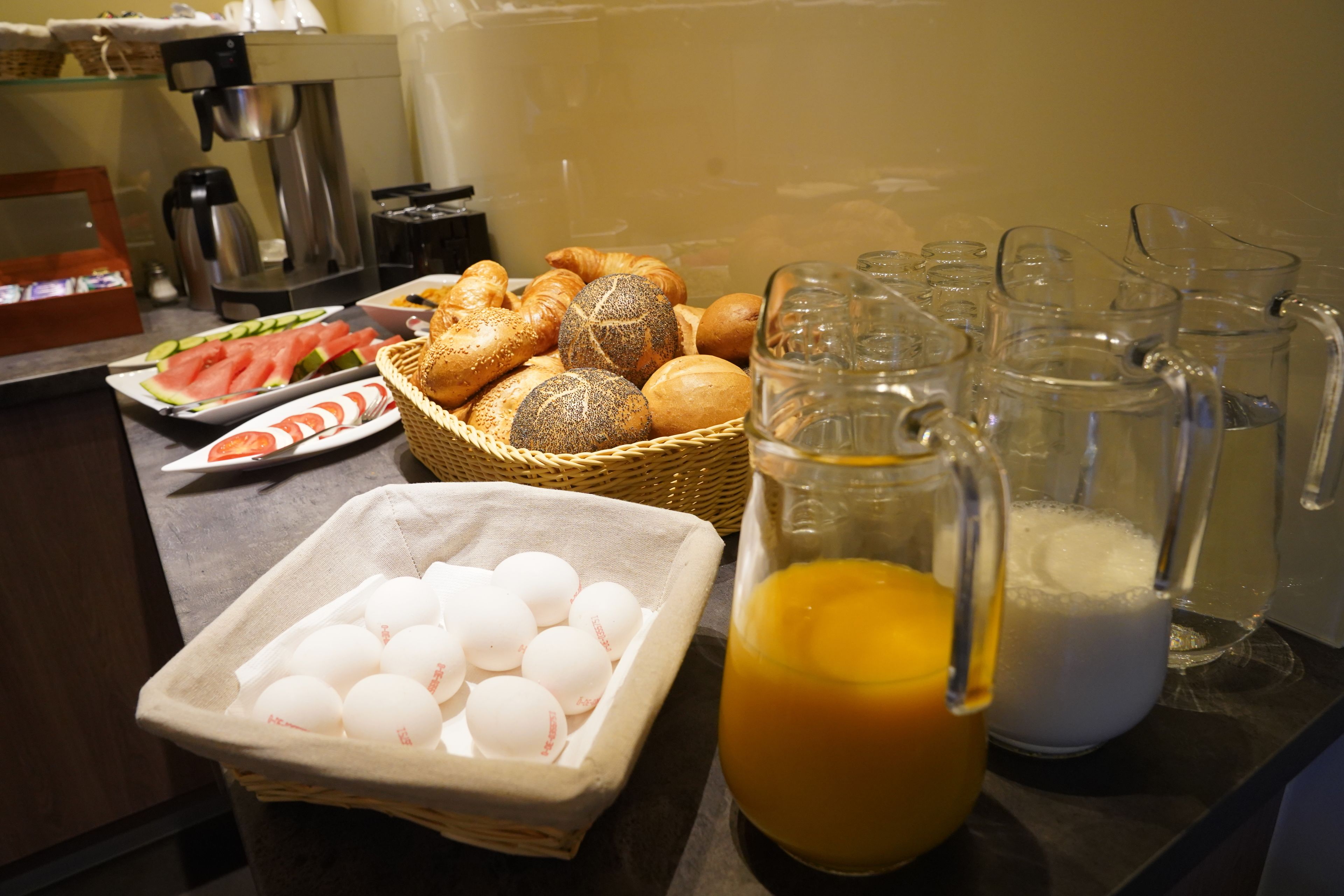 A breakfast buffet with bread, pastries, eggs, and beverages.