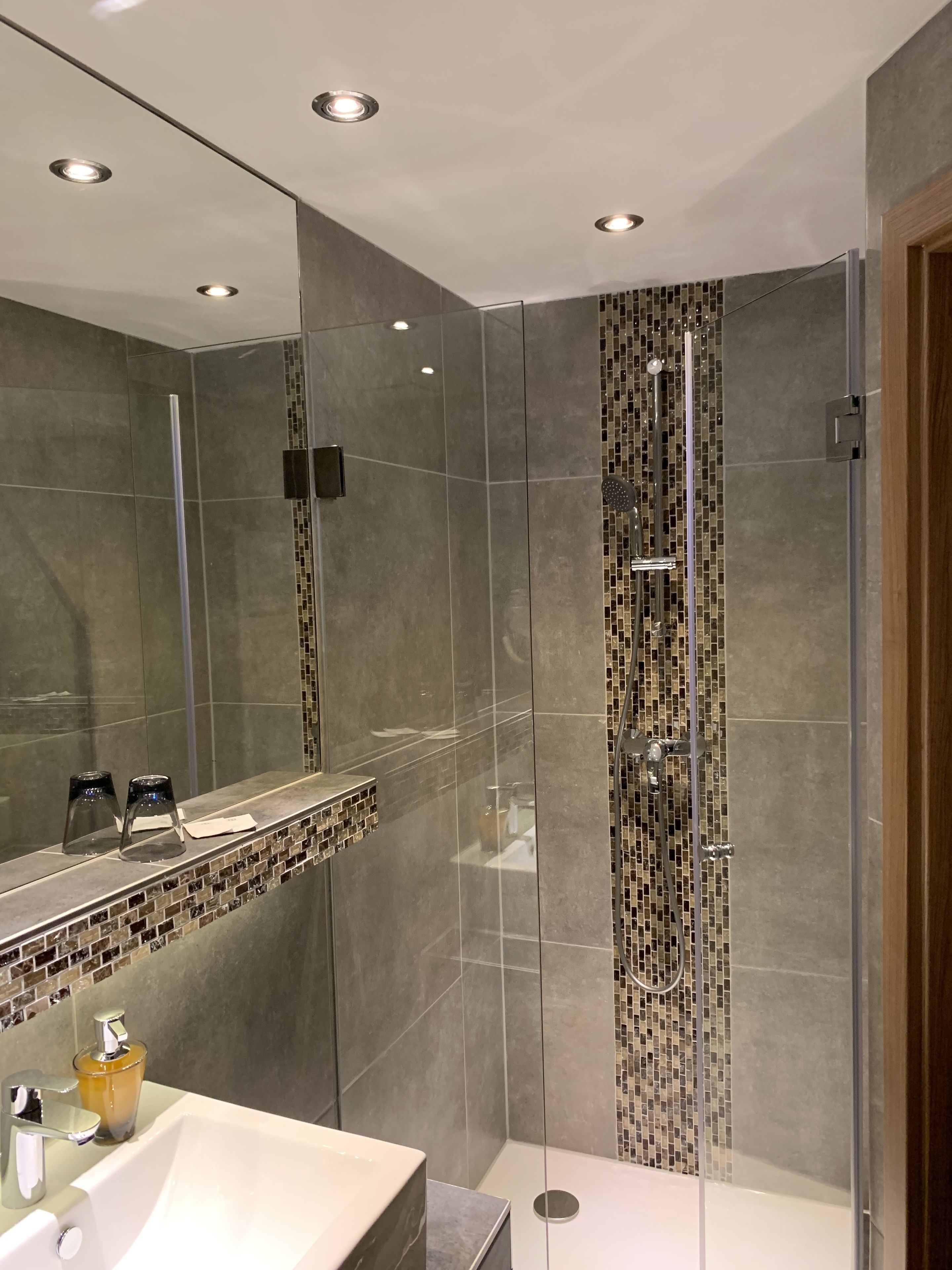 A modern bathroom with a glass-enclosed shower, a large mirror, and a sink with a chrome faucet.