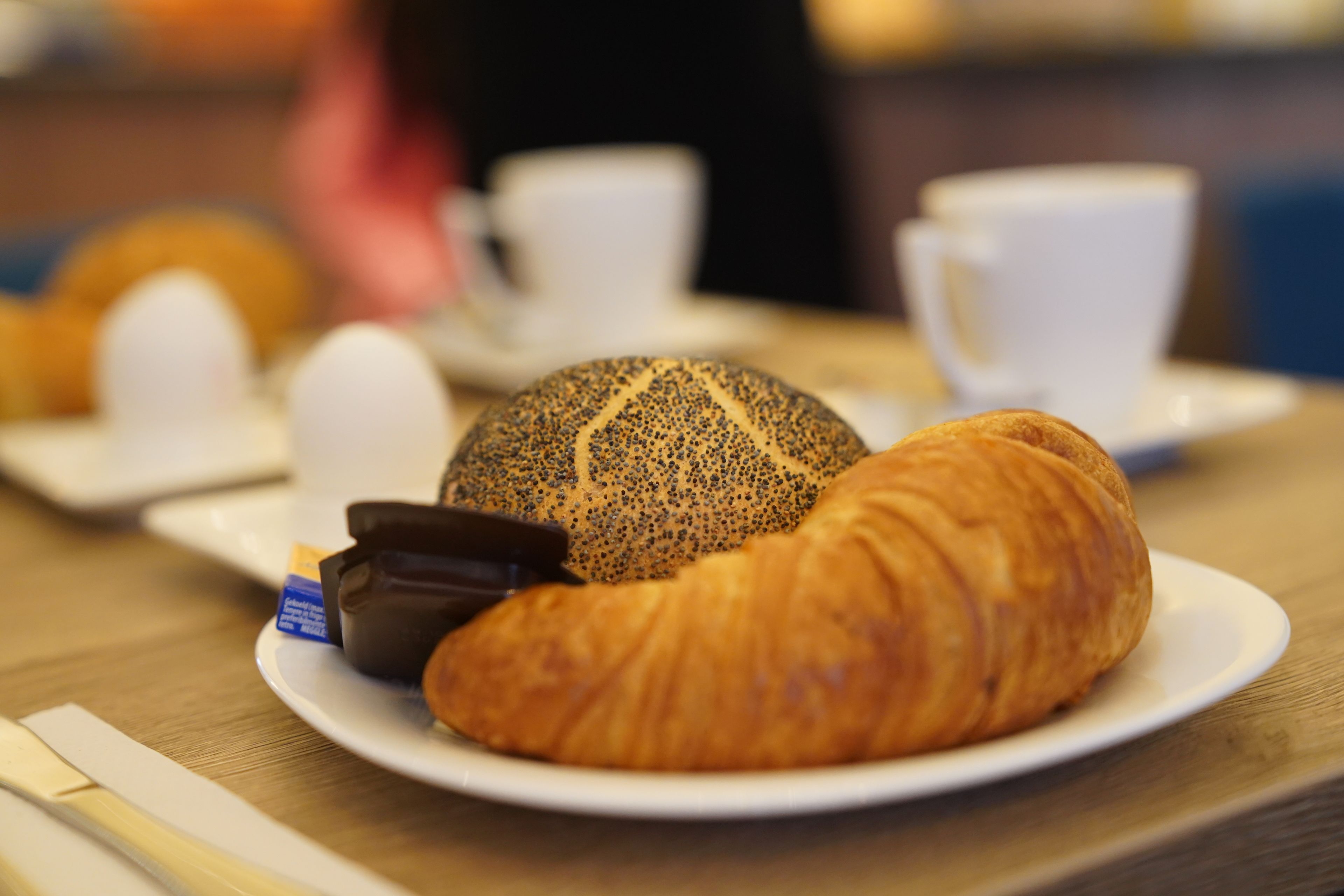 A plate with a croissant and a chocolate bar on a wooden table.