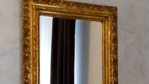 Een spiegel aan de muur, voorzien van een sierlijke gouden lijst.