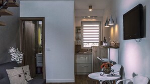 Een knus woongedeelte met een bank, een eettafel met stoelen, een keuken en een aan de muur bevestigde televisie.