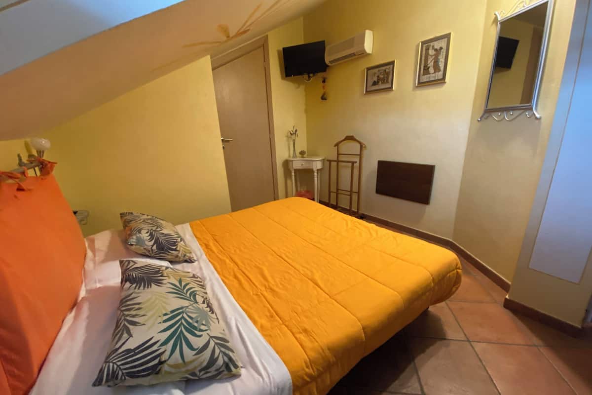 Quarto com cama, mesa de cabeceira, televisão na parede e espelho.