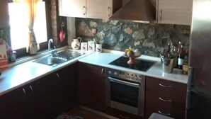 Ett kök med träskåp, en stänkskydd av sten, en rostfri köksfläkt, en inbyggd ugn och ett kylskåp.