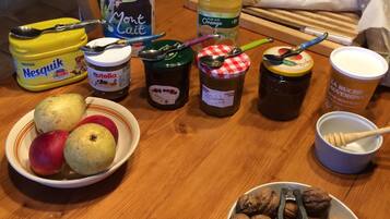 Ein Holztisch mit verschiedenen Speisen, darunter Äpfel, Walnüsse, Nutella und Gläser mit Marmelade.