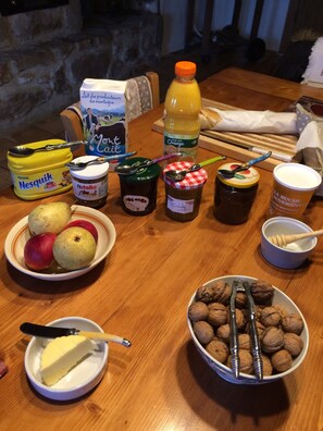 A wooden table with various food items including apples, walnuts, Nutella, and jars of preserves. - Chambre d'hôte la Fessille (Fayet-Ronaye)