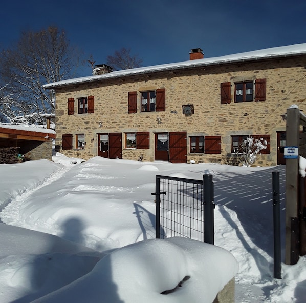 A stone building with multiple windows and doors, surrounded by snow. - Chambre d'hôte la Fessille (Fayet-Ronaye)