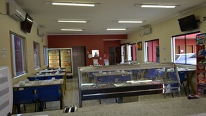 A cafeteria with tables and chairs, a display case, and a television on the wall. - Hotel Poloni (Itapetininga)