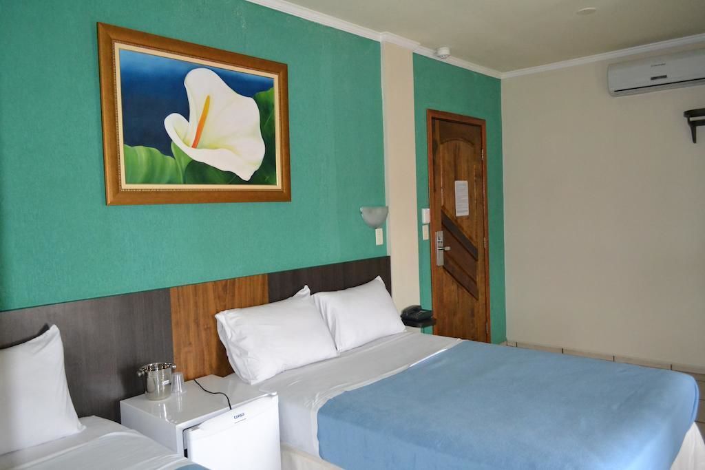 Ett hotellrum med en säng, sängbord, ett litet bord, en inramad tavla och en dörr.