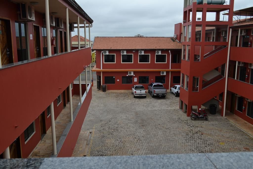 A multi-story building with a red exterior, a covered parking area, and a cobblestone ground.