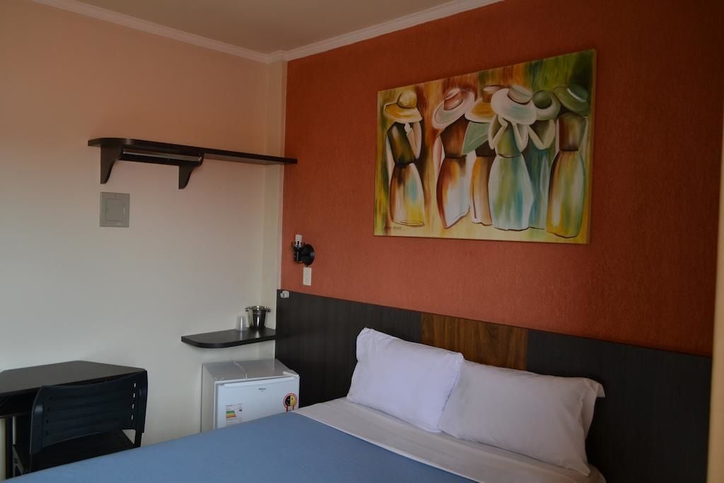 Hotelkamer met een bed, bureau, kleine koelkast en een schilderij aan de muur.