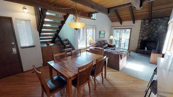 A spacious living area with a wooden dining table, comfortable seating, a fireplace, and a staircase leading to an upper level.