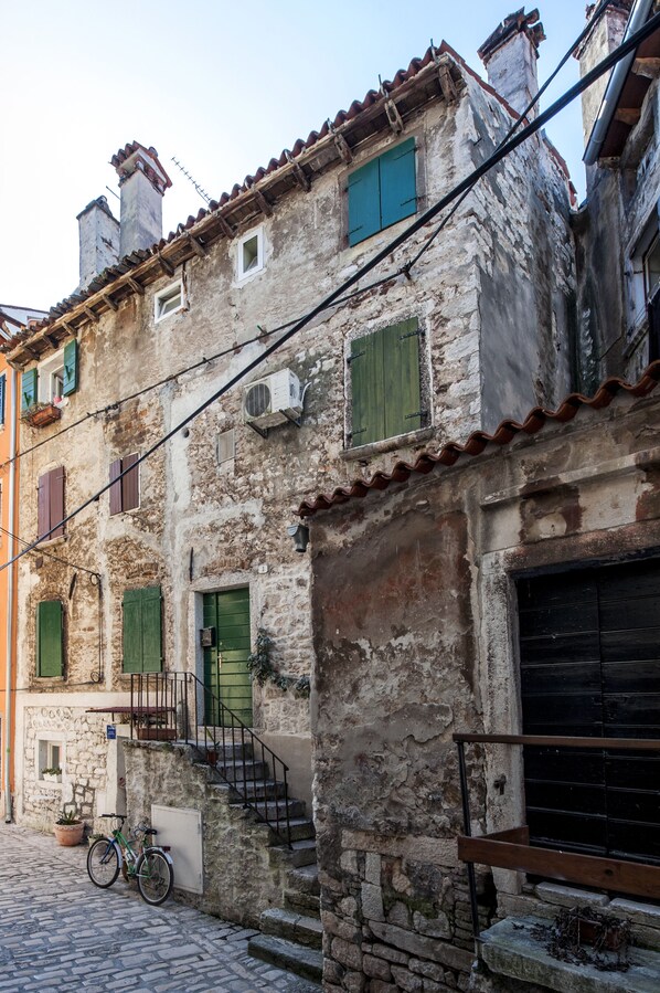 A narrow cobblestone street with a rustic stone building featuring a staircase, a bicycle, and a potted plant. - Pisinium Studios (Rovinj)
