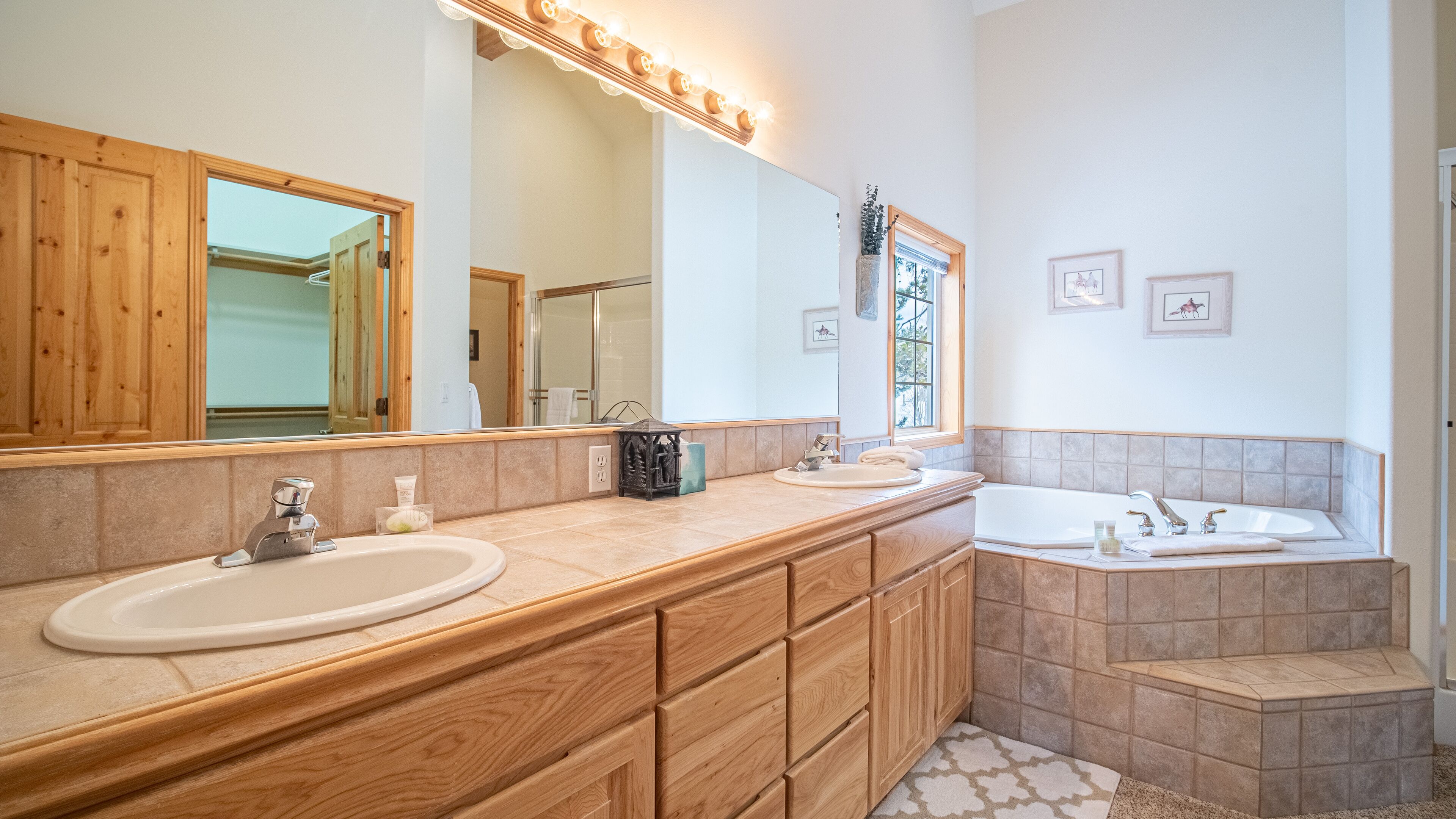 A bathroom with wooden cabinetry, a double sink vanity, a large mirror, and a bathtub.
